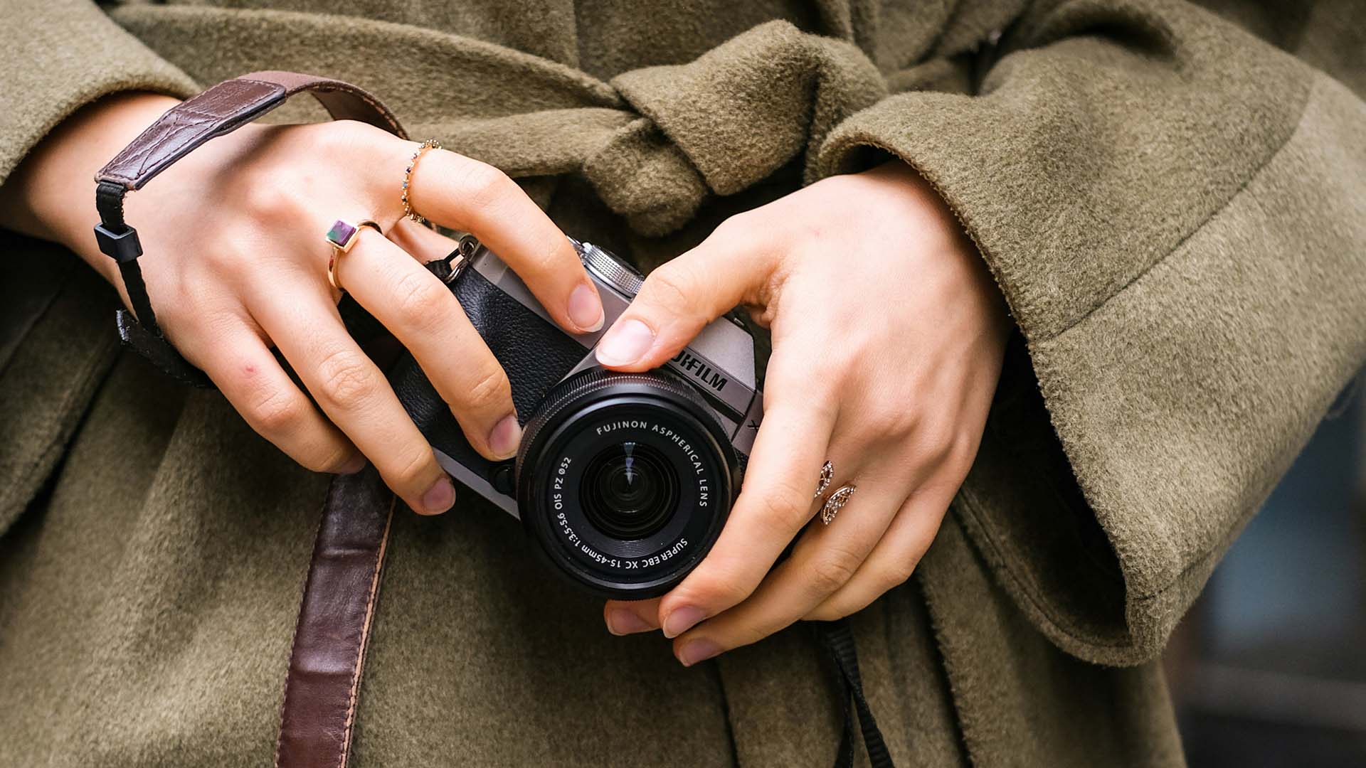 Person in overcoat with jewelry holding camera.