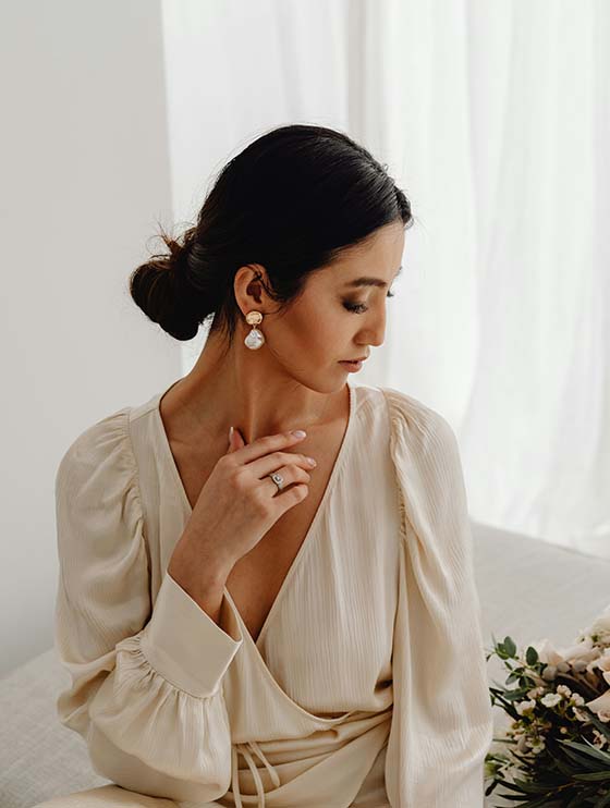 Person in elegant clothes and jewelry sitting in front of window.