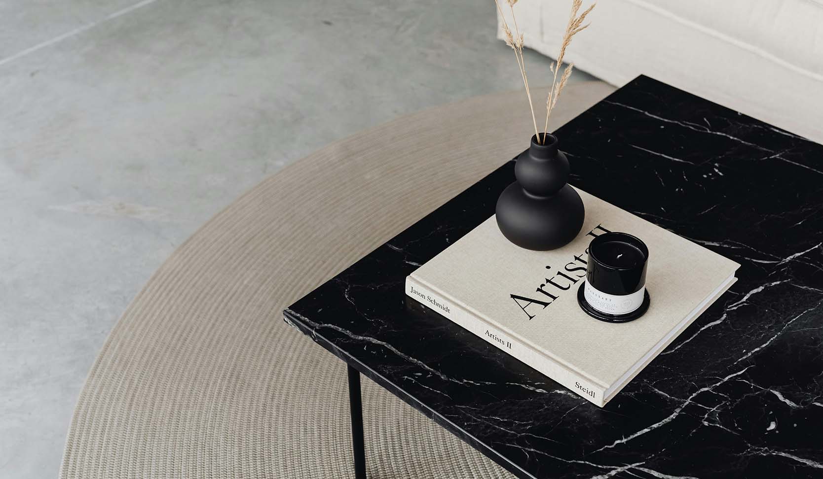Black stone table with coffee table book, vase with plants, and candle.